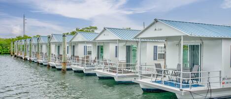 A row of floating cottages with balconies and outdoor seating, docked along a waterway.