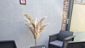 Un espace patio aménagé avec des meubles en osier, comprenant deux chaises et une petite table, ainsi qu’une plante décorative.