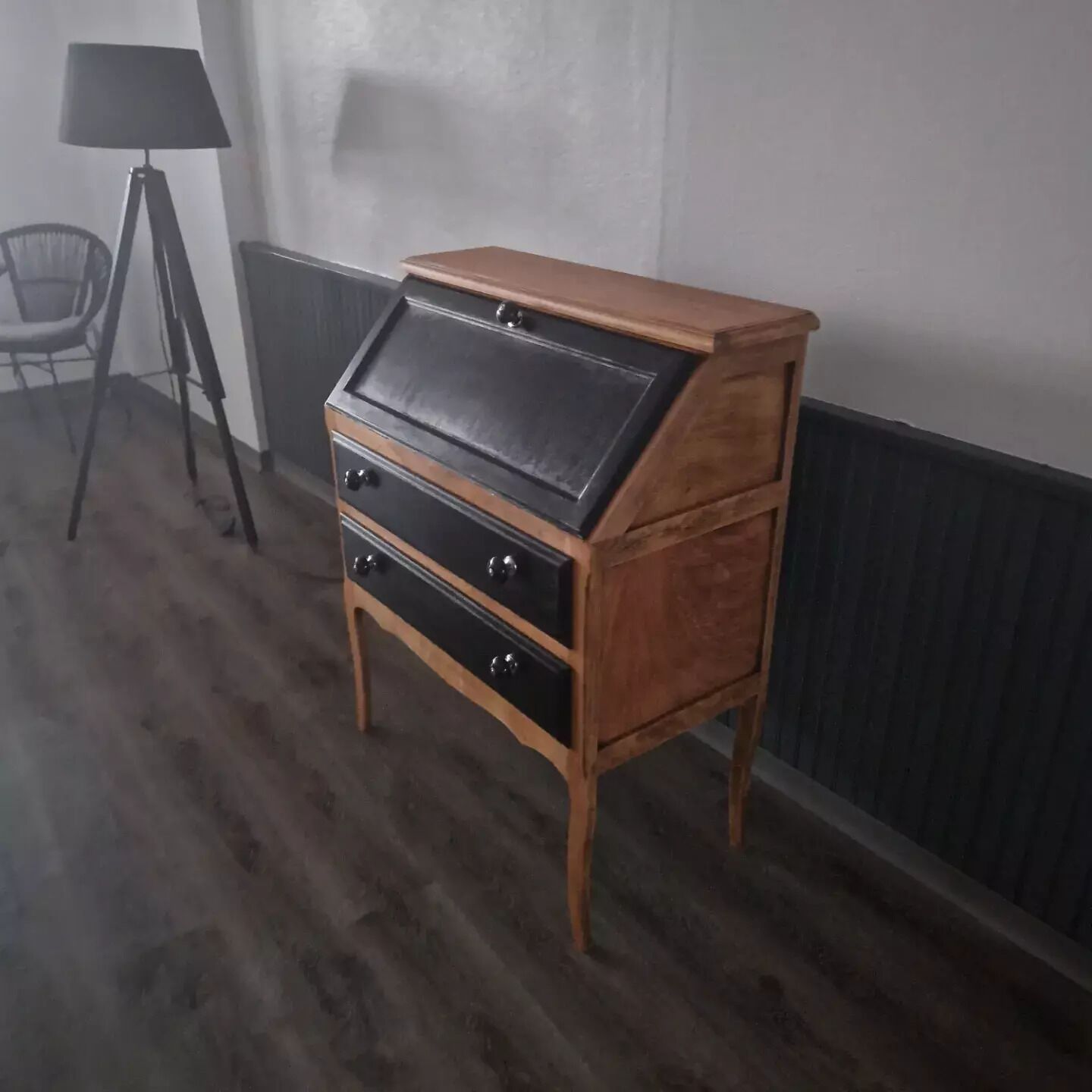 A wooden chest of drawers with a black top, positioned in a room with a radiator and a chair.