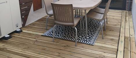 A patio with a table and chairs, a grill, and a glass door leading to a covered area.