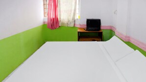 Une pièce avec un lit, un téléviseur posé sur un meuble en bois et une fenêtre avec un rideau.