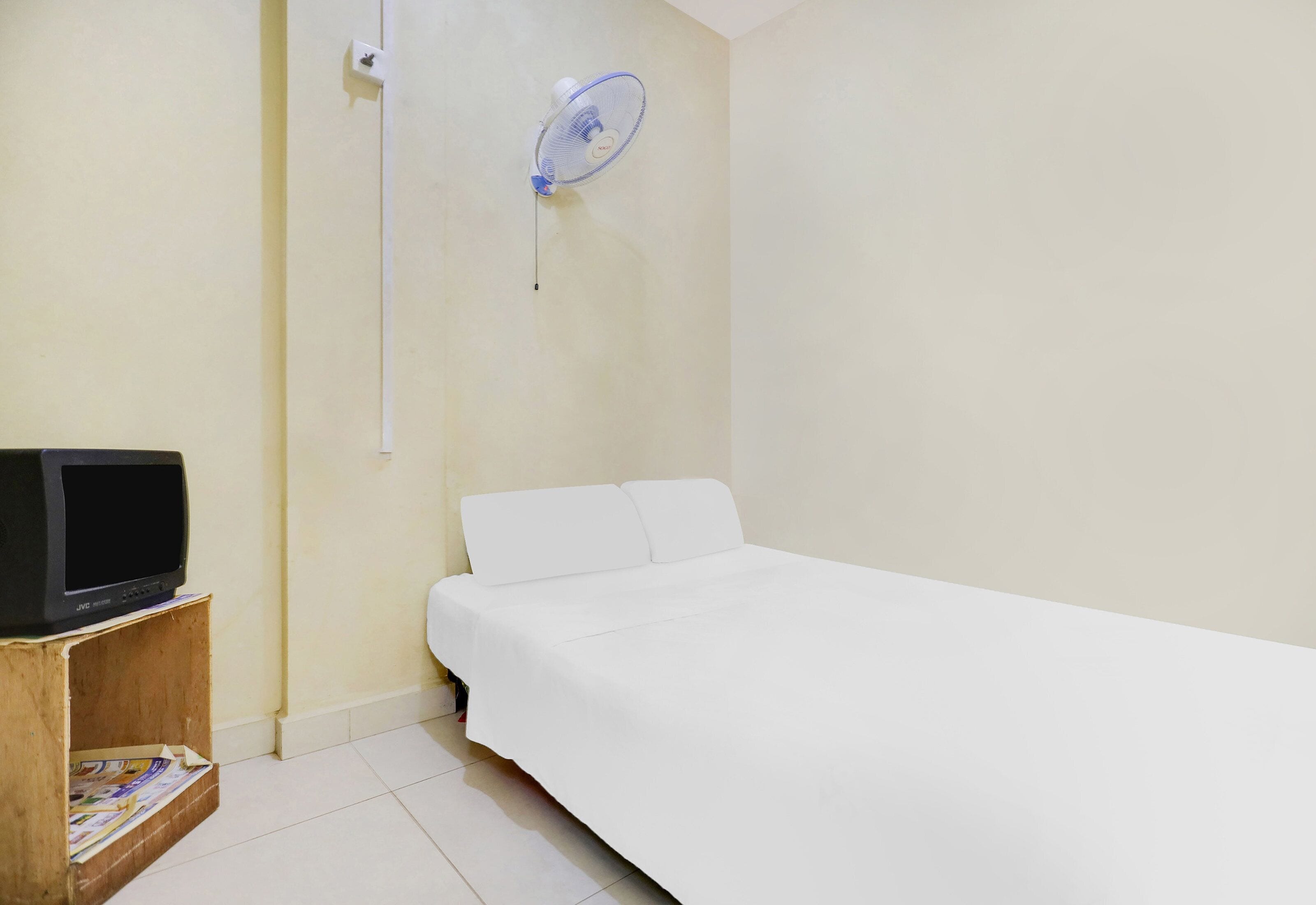 A room with a bed, a small wooden table with a television, and a wall-mounted fan.