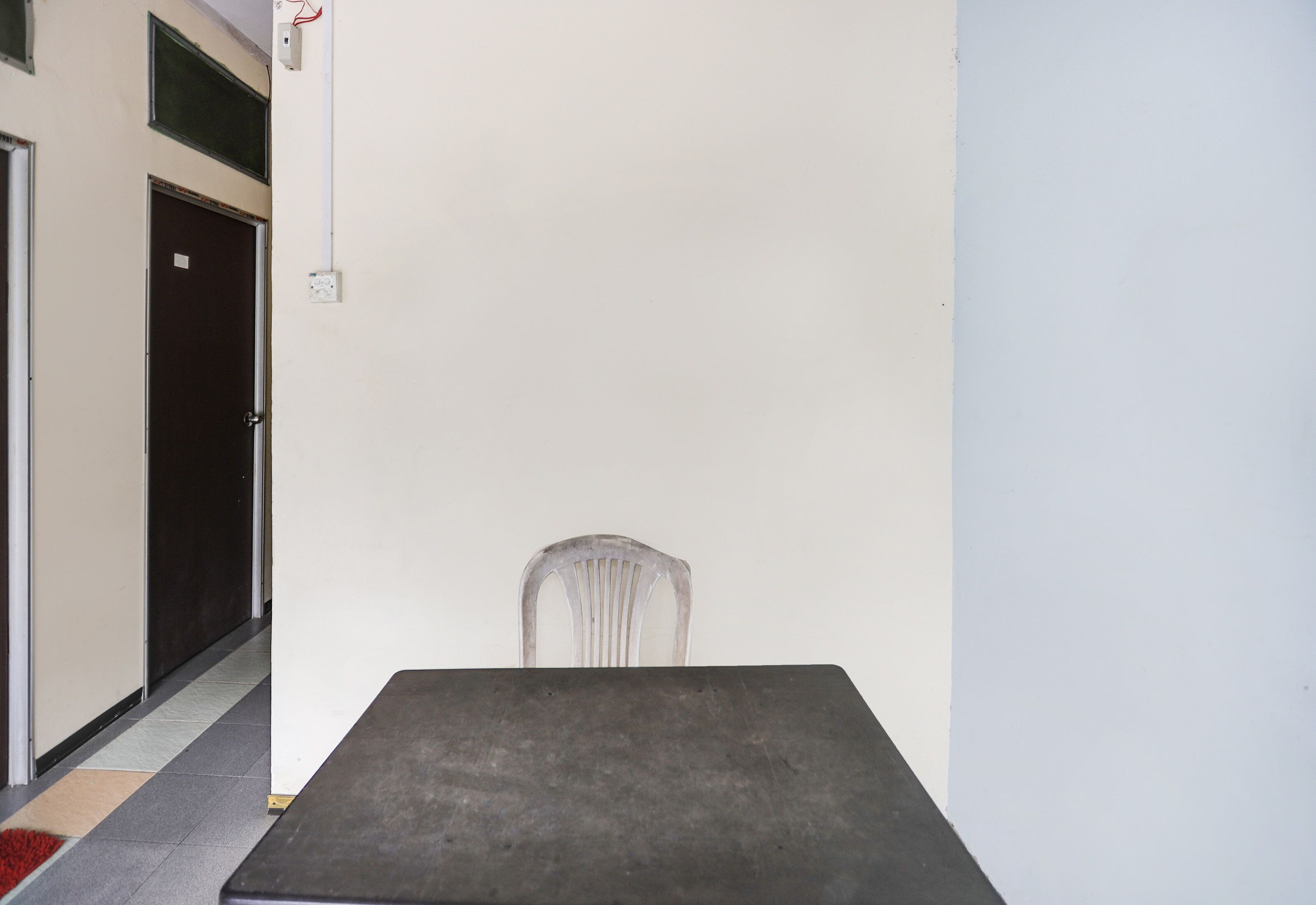 A room with a single table, a chair, a door, and a wall socket.