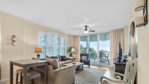 A spacious living room with a large window, a ceiling fan, and a dining area with bar stools.
