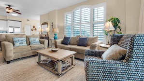 A spacious living room with a beige sofa, a patterned armchair, and a coffee table.
