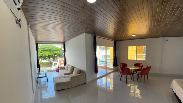 Une pièce spacieuse dotée d’un plancher ciré, d’un canapé, d’une table à manger avec des chaises et de grandes fenêtres offrant une vue sur l’extérieur.