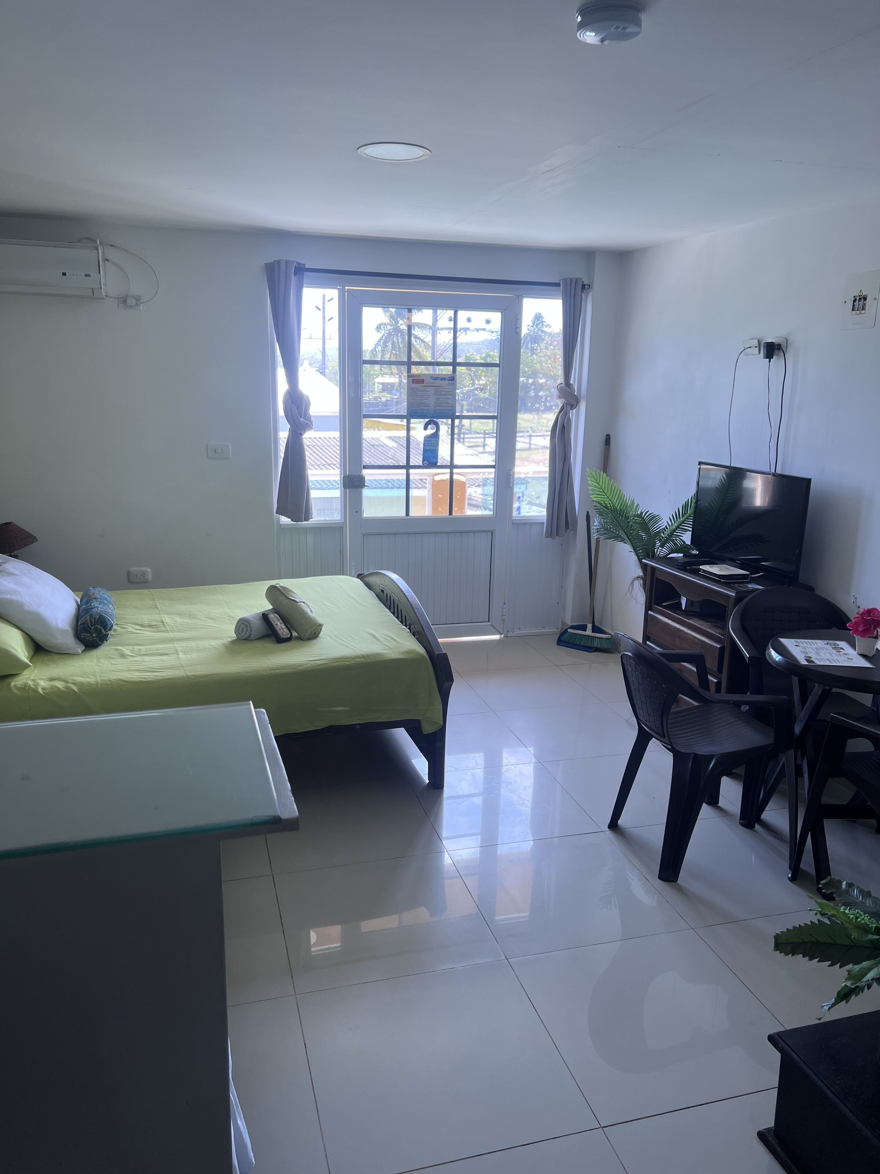 Habitación de hotel con cama, escritorio con computadora, televisor y ventana con cortinas.