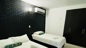 Une chambre avec deux lits, un mur en briques noires, un climatiseur et une armoire.