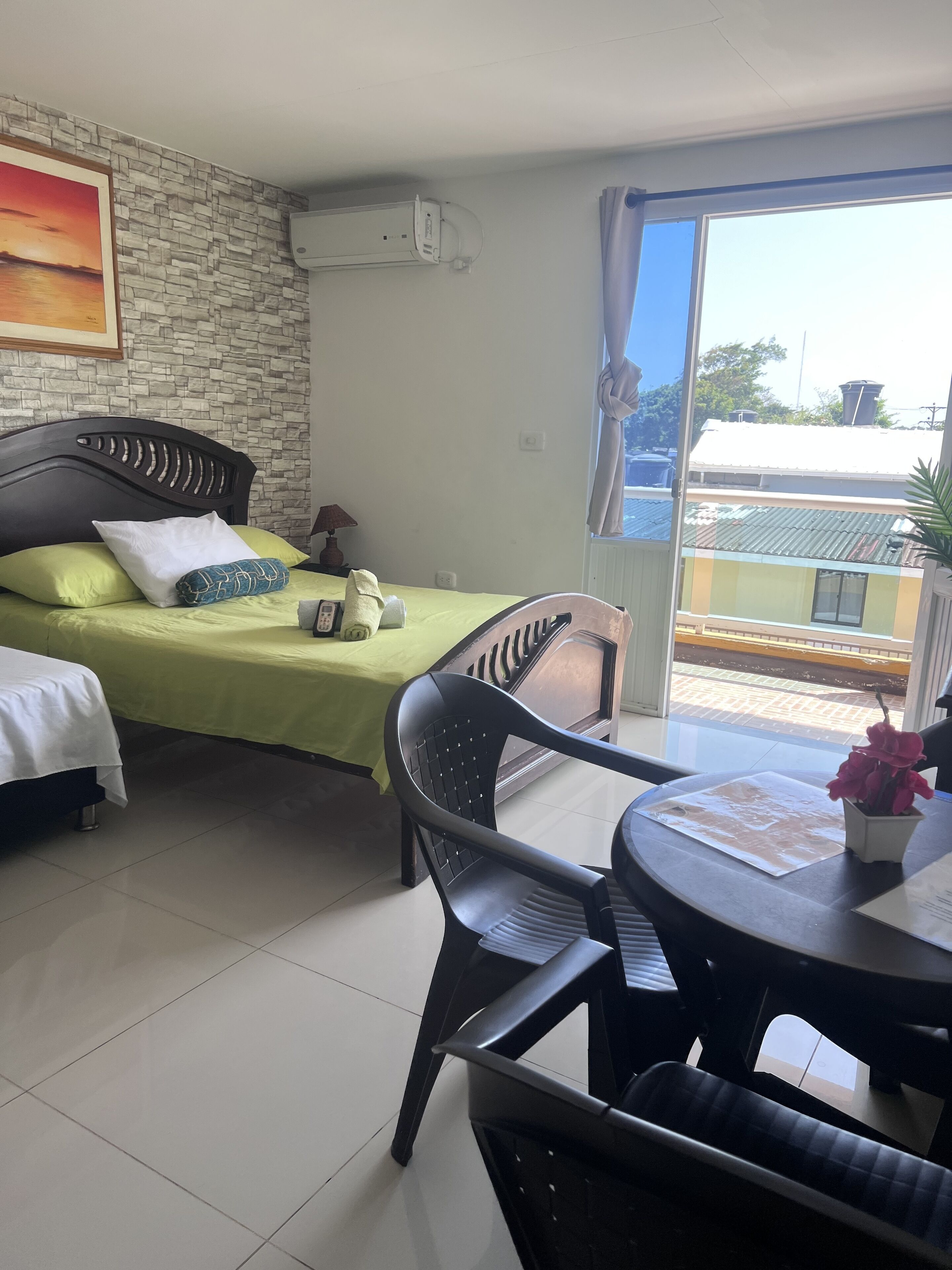 A hotel room with a bed, a chair, a table, and a view of the outside.