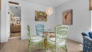 A dining area with wicker chairs, a glass table, and a hanging light fixture. - 🏝️In the Heart of Navarre-Bungalow By the Sea-Mermaid (Navarre)