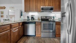 A modern kitchen with wooden cabinets, stainless steel appliances, and a dishwasher. - 🏝️In the Heart of Navarre-Bungalow By the Sea-Mermaid (Navarre)