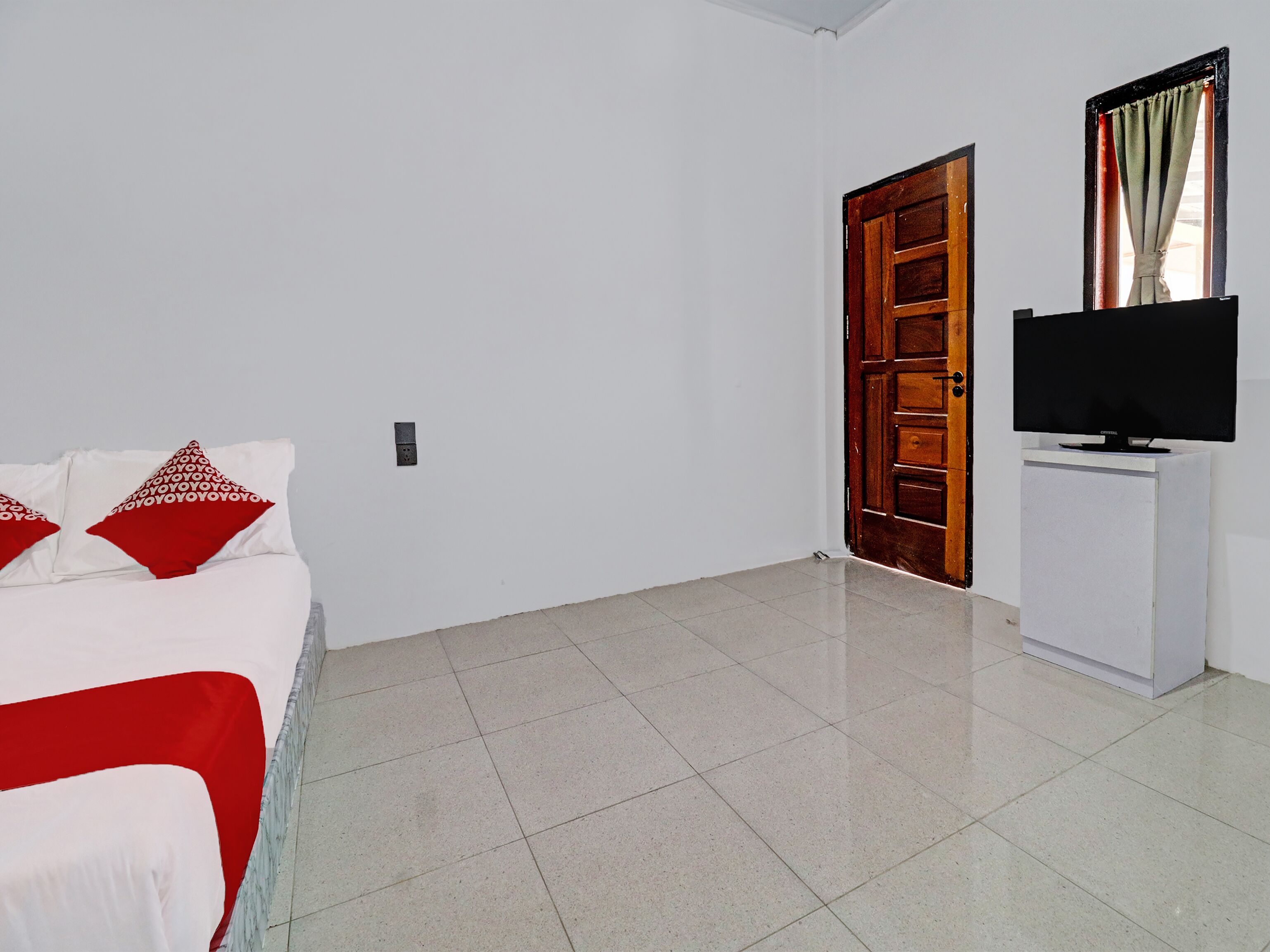 A hotel room with a bed, a television on a stand, and a door.