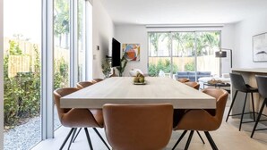 A modern dining area with a large table and chairs, large windows, and a view of the outdoors. - Modernista, Luxury Villa, Pool by Coconut Grove (Miami)