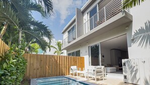Ein modernes, zweistöckiges Haus mit Pool, Gartenmöbeln und Holzzaun.