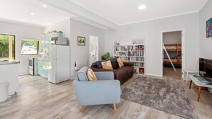 A modern living space with a kitchen, dining area, and a cozy seating area with a sofa and a bookshelf. - Waitahanui Lake House - Lake Taupo Holiday Home (Waitahanui)