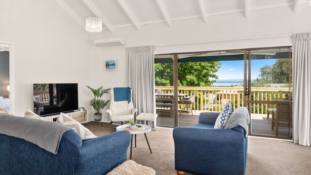 A spacious living room with a large TV, comfortable seating, a small table, and a view of the outdoors. - Waitahanui Lake House - Lake Taupo Holiday Home (Waitahanui)