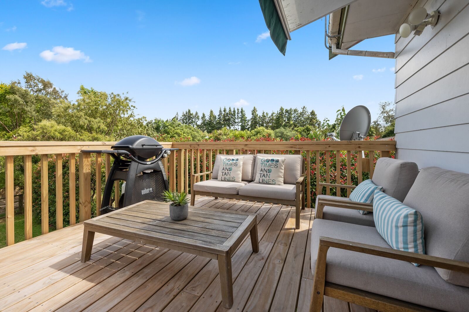 Una terraza de madera con una parrilla, un sofá con cojines, una mesa y una planta en maceta.