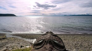 A beach with a rocky foreground and a calm sea under a partly cloudy sky. - Waitahanui Lake House - Lake Taupo Holiday Home (Waitahanui)