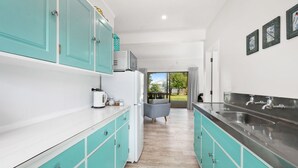 A modern kitchen with teal cabinetry, a stainless steel sink, and a view to the outdoors. - Waitahanui Lake House - Lake Taupo Holiday Home (Waitahanui)