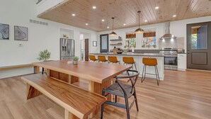 Una cocina amplia con una mesa y sillas de madera, electrodomésticos de acero inoxidable e iluminación colgante.