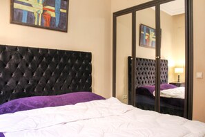 A bedroom with a tufted headboard, a bed with white and purple bedding, and a large mirror reflecting the room. - Cosy Place in the heart of Gueliz Marrakech (Marrakech)