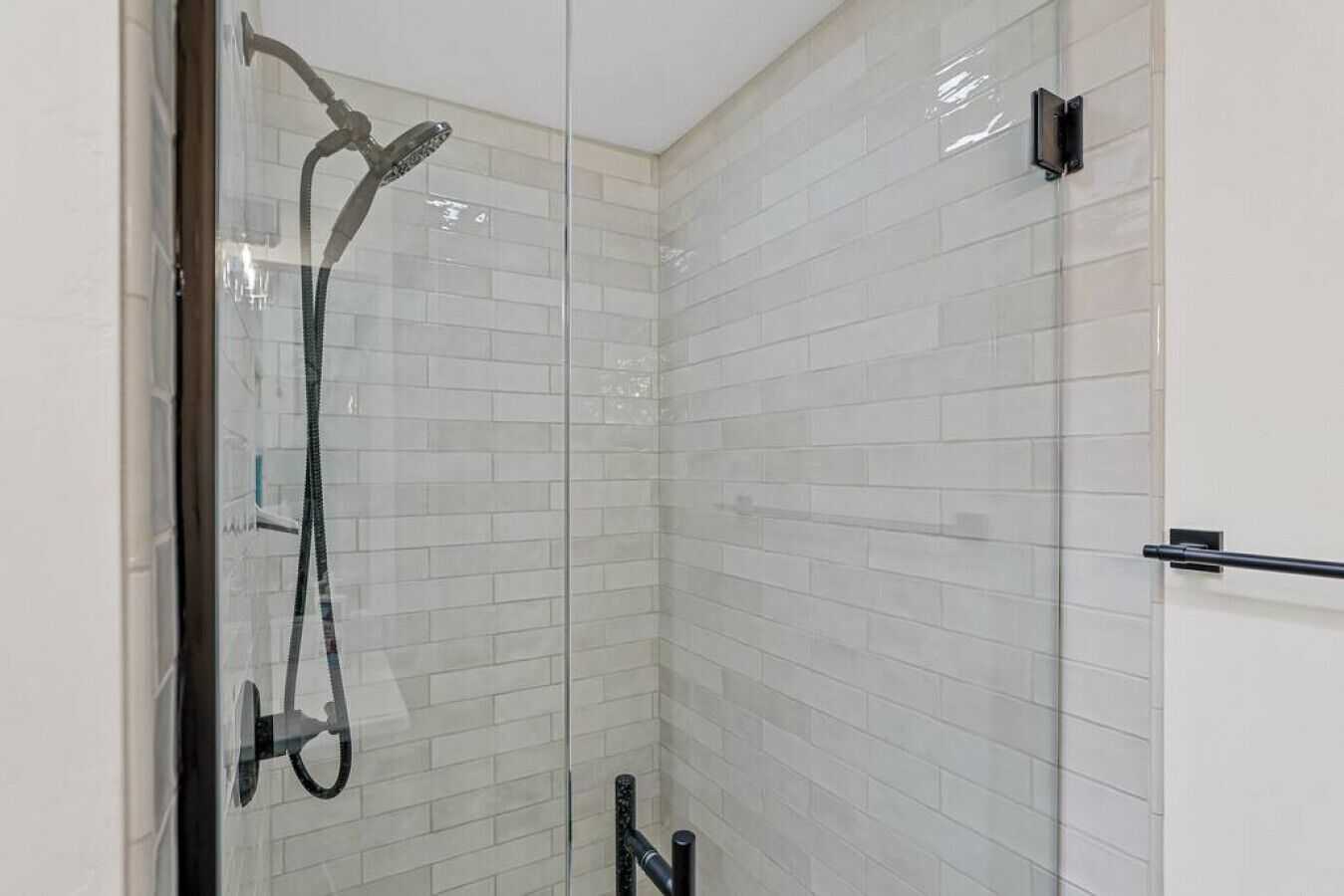 A glass-enclosed shower with a handheld showerhead and a wall-mounted faucet.