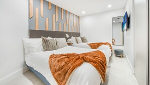 Une chambre moderne avec deux lits, un mur d’accent en bois, un petit tabouret et un téléviseur fixé au mur.