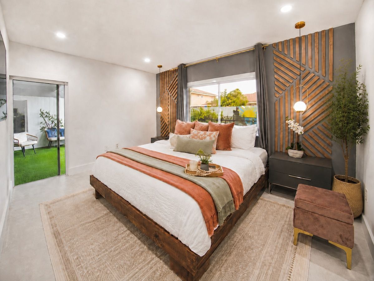 Un dormitorio moderno con una cama grande, mesitas de noche, una planta en maceta y vistas al exterior.