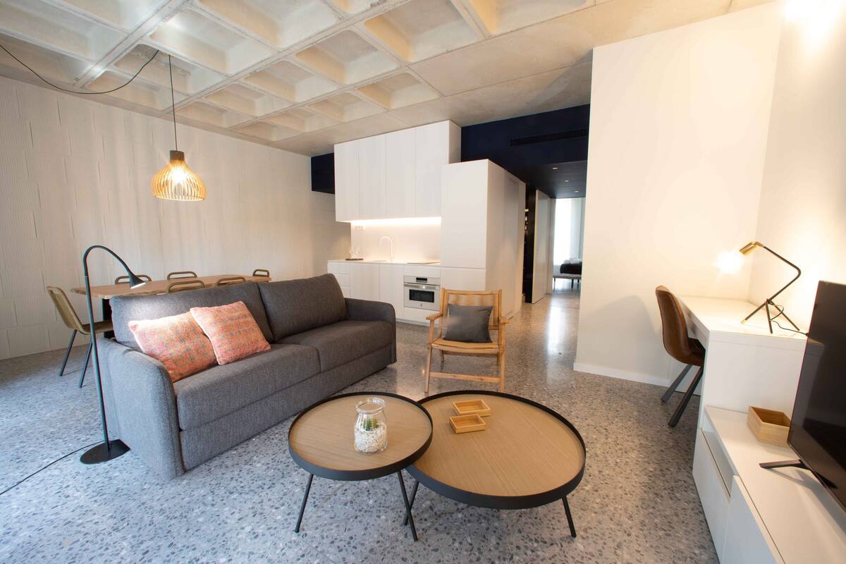 A modern living room with a grey sofa, two round coffee tables, and a dining area with a wooden table and chairs.