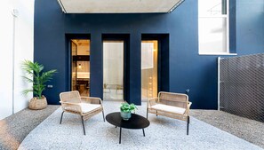 A modern outdoor seating area with wicker chairs and a central table, a dark blue wall, and a glass door leading to an interior space.