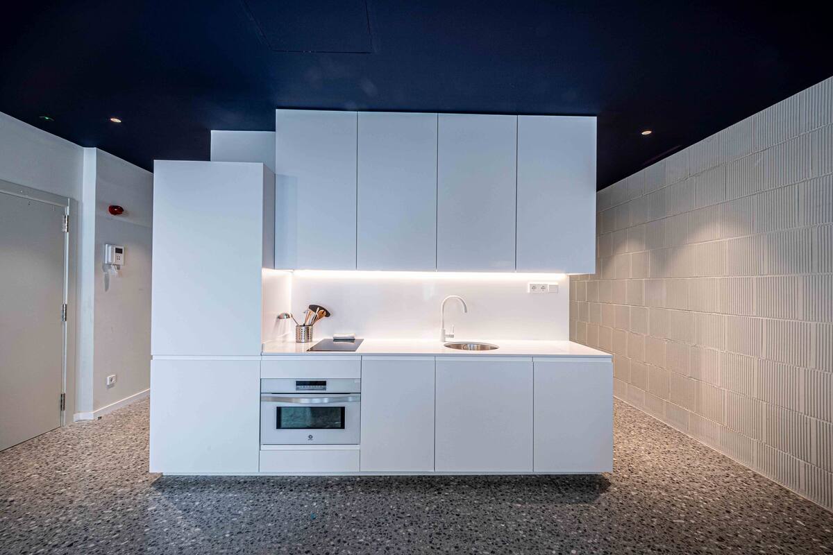 A modern kitchen with white cabinetry, a built-in oven, and a stainless steel sink.