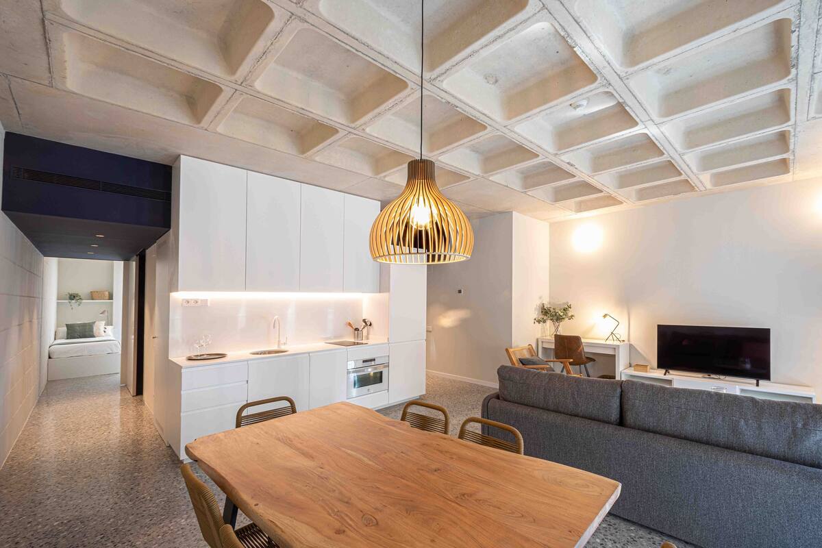 A modern kitchen with white cabinets, a wooden dining table, and a hanging pendant light.