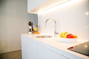 A modern kitchen with a white countertop, stainless steel sink, and a bowl of fruit.