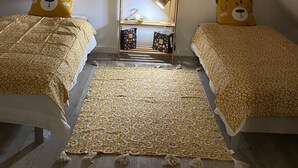 A cozy attic bedroom with two beds, a wooden shelf with decorations, and a patterned rug. - Spacious self-catering cottage near the beach for 16 people COTE DE GRANIT ROSE (Pleubian)