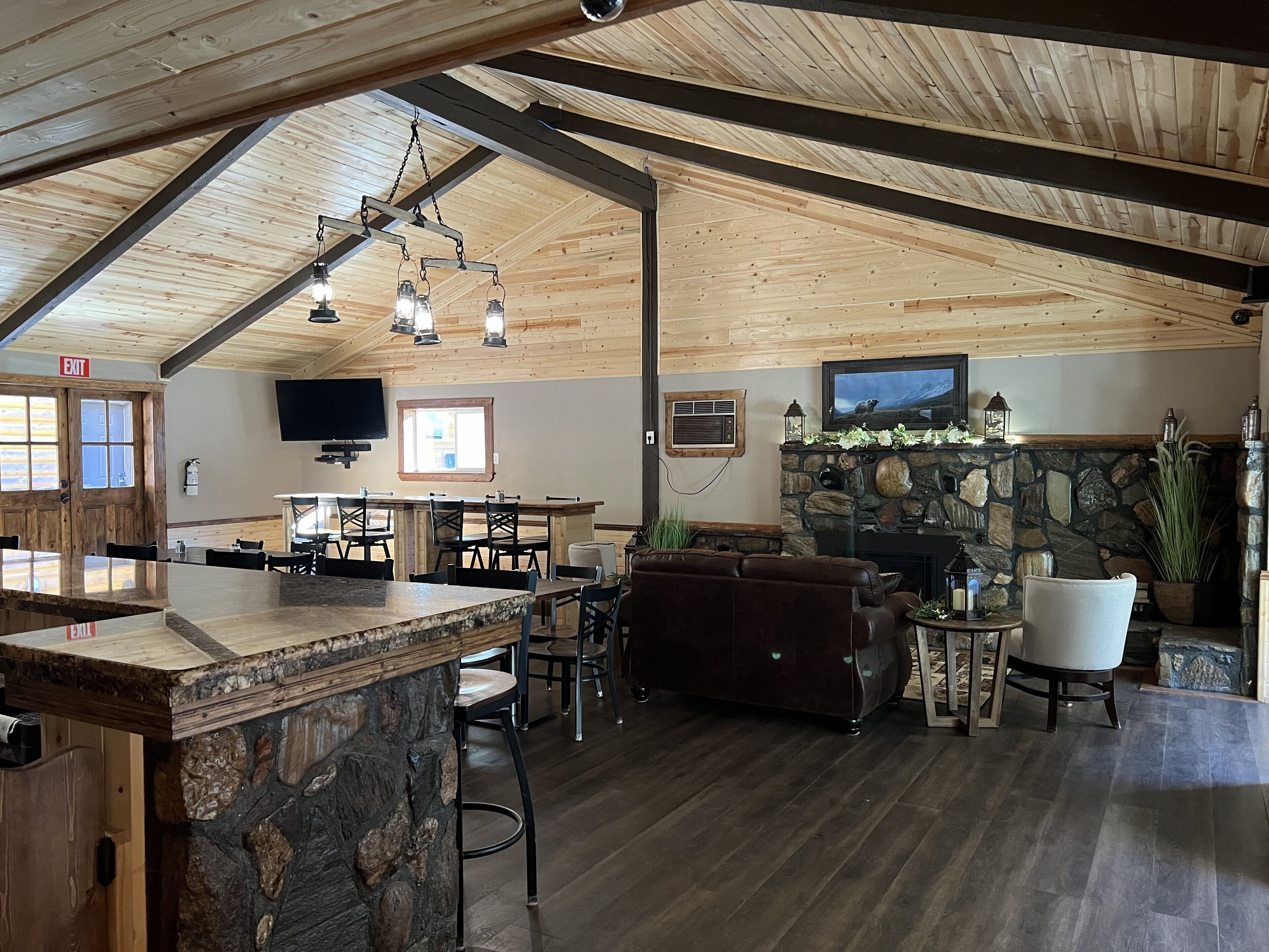 A spacious interior with a high ceiling, a stone fireplace, a television mounted on the wall, and a bar area.