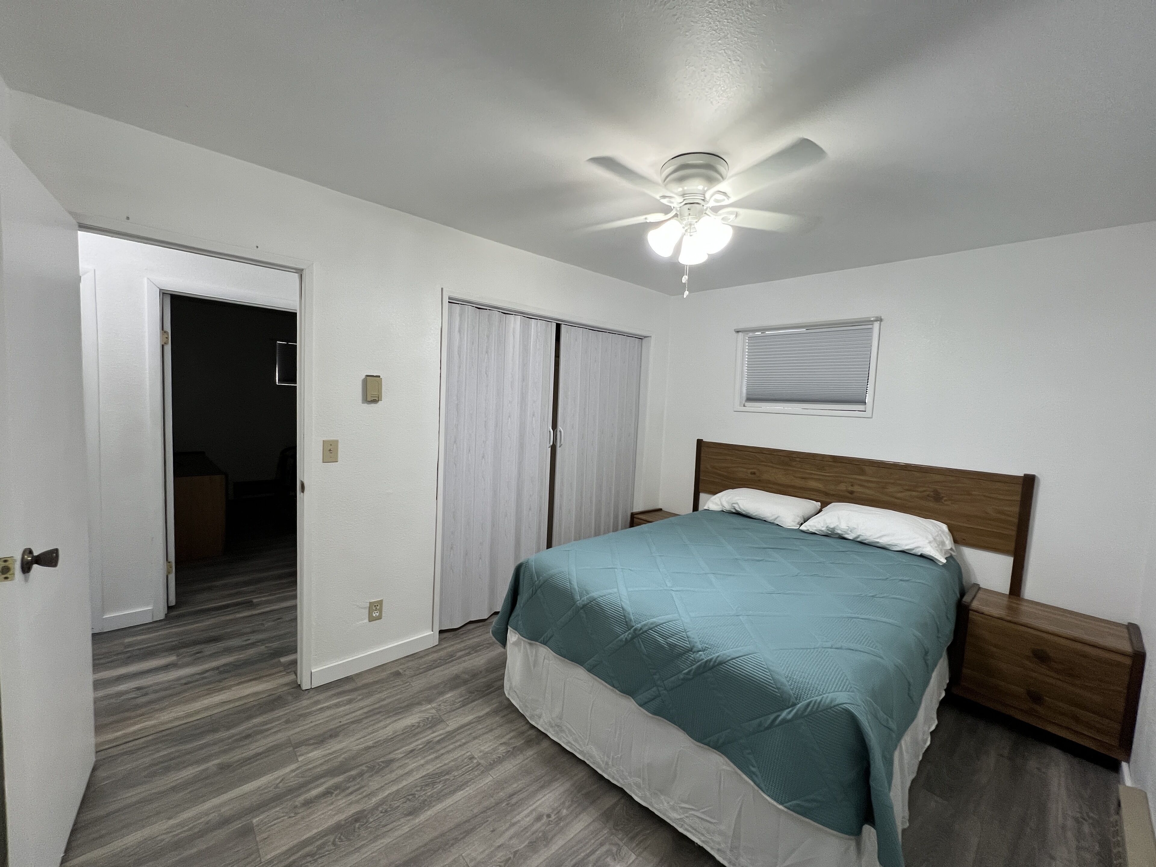 A bedroom with a bed, wooden headboard, nightstands, a ceiling fan, and a window with blinds.