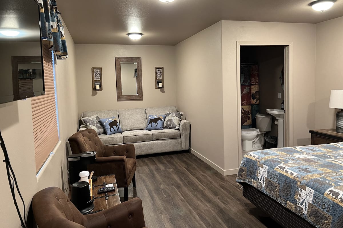 A hotel room with a sofa, armchairs, a bed, a desk, and a bathroom.