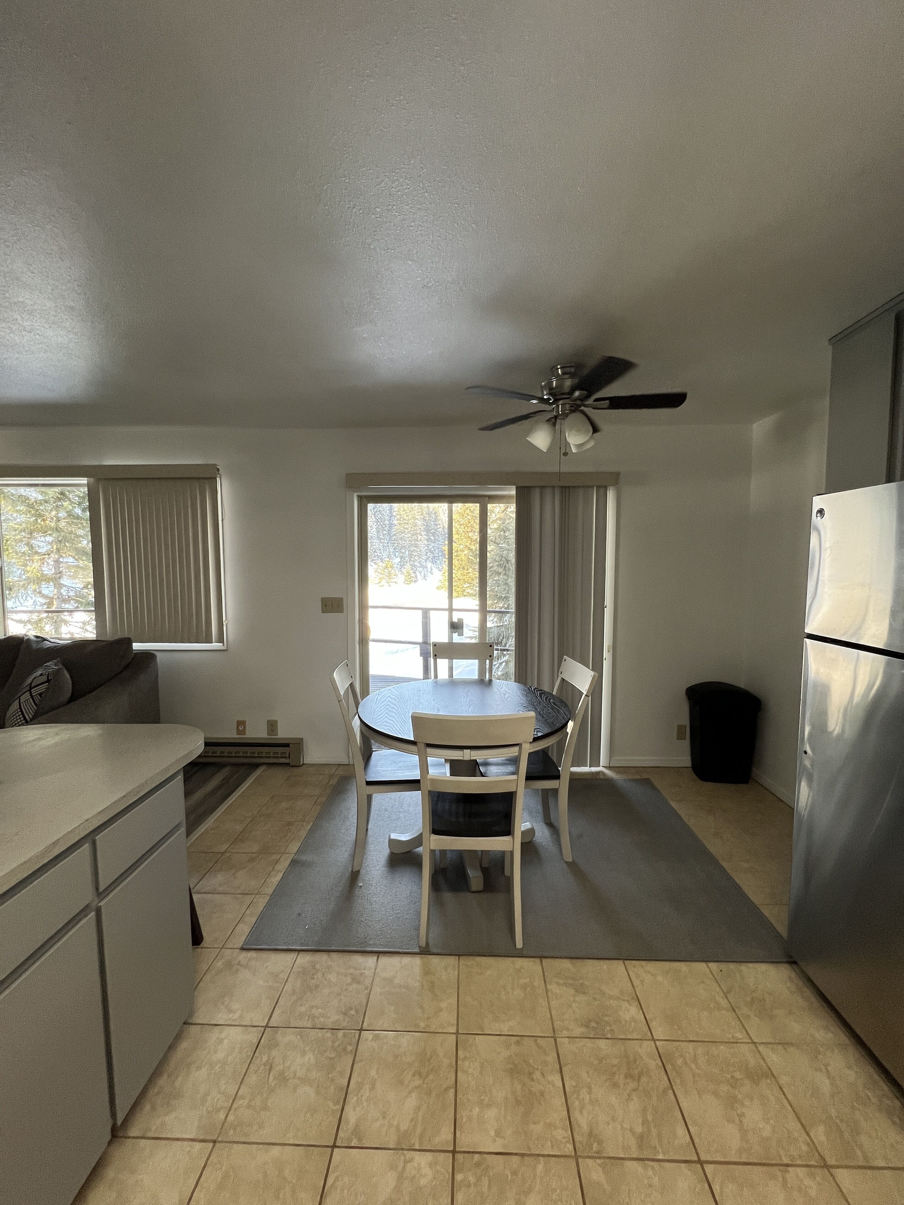 A compact kitchen with a dining table, chairs, a ceiling fan, and a refrigerator.