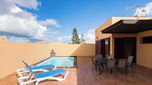 A rooftop pool area with blue lounge chairs, a dining table with chairs, and a small garden with a tree. - Home2Book Isla Lagoa, Private Pool (La Oliva)