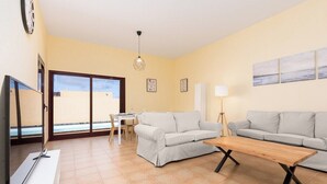 A living room with two sofas, a wooden coffee table, a TV, and a dining area with a table and chairs. - Home2Book Isla Lagoa, Private Pool (La Oliva)
