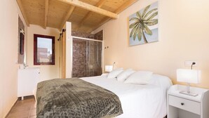 A bedroom with a large bed, a nightstand, a lamp, a painting of a palm tree, and a shower area. - Home2Book Isla Lagoa, Private Pool (La Oliva)