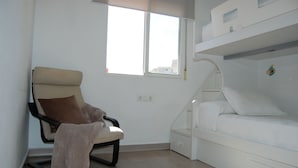 Ein Zimmer mit einem Etagenbett, einem Stuhl mit Decke und einem Fenster.