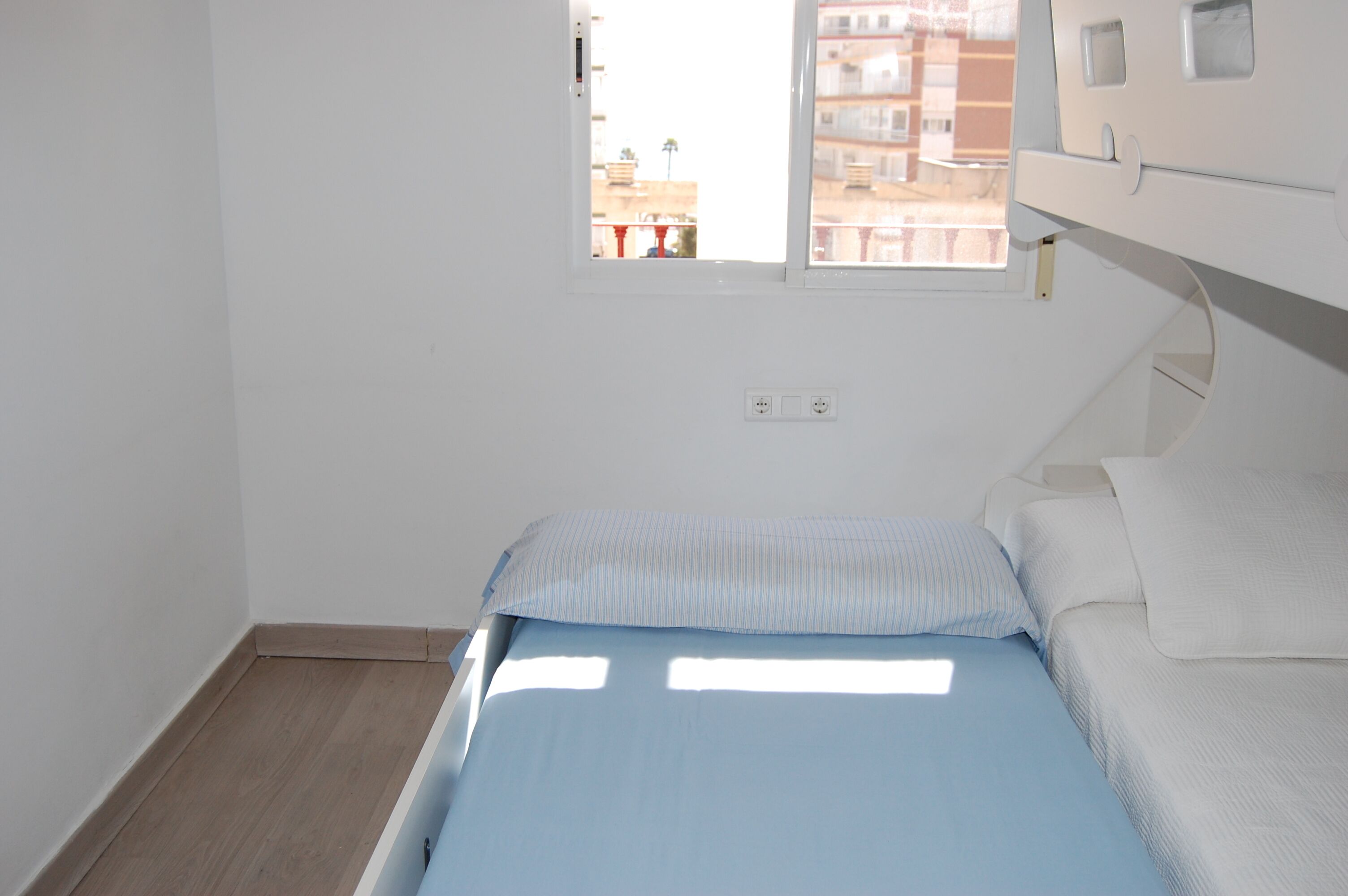Ein kleiner, heller Raum mit einem Bett, einem Fenster und Holzboden.