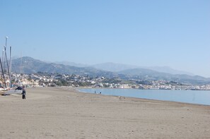Ein weiter Sandstrand mit Booten und einer entfernten Stadtansicht.