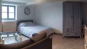 A bedroom with a bed, a glass coffee table, a wardrobe, and a desk.