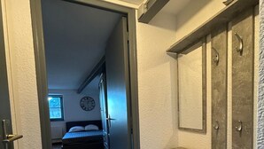 A narrow hallway leading to a bedroom with a bed and a clock on the wall.