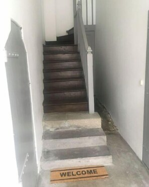Stairs lead to an upper floor, flanked by a welcome mat and a door.