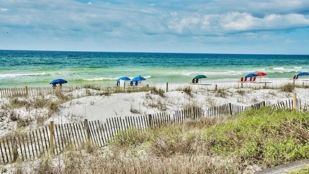 A beach with wooden fences, umbrellas, and people relaxing.