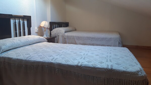 Two beds with white, textured bedding and fringed edges, a wooden headboard, and a nightstand with a lamp.