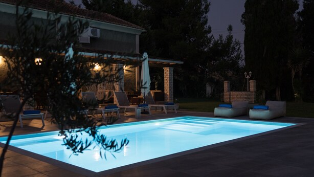 Una piscina con sillones de descanso y un patio cubierto.